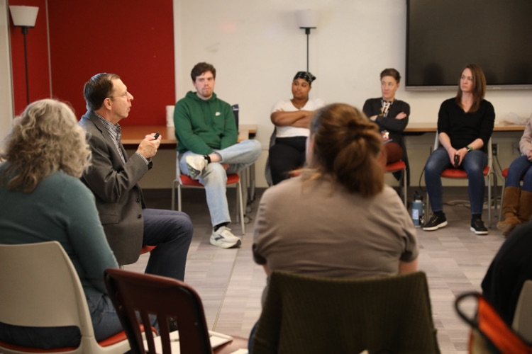  Educators sit in a circle during a workshop session, listening and engaging in a group discussion led by a facilitator.