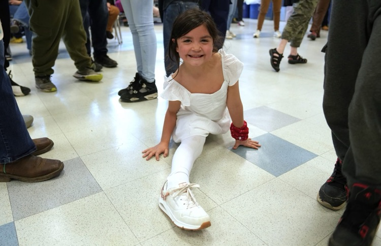 One small student smiling at the camera while performing a split on the floor