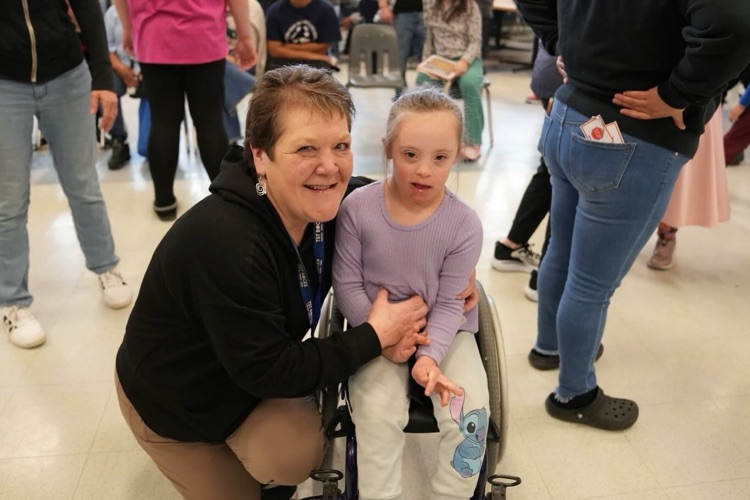 a TST staff crouches down and smiles with student in wheelchair out on the dance floor