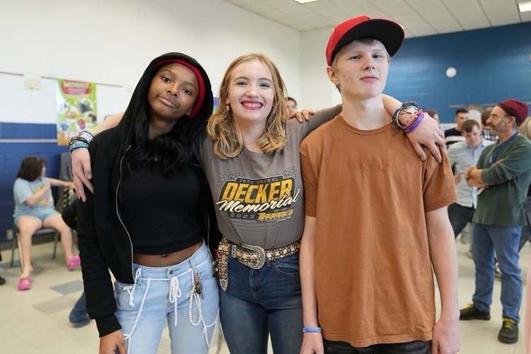 three students with arms around each other smiling at camera on dance floor