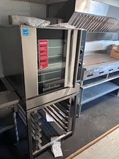 Commercial convection oven next to stainless steel cooking equipment and ventilation hood inside the trailer.