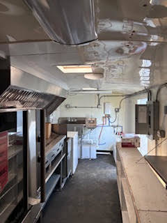 Wide view of the trailer interior featuring stainless steel counters, appliances, sink area, and electrical panel.