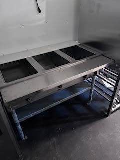 Large flat top grill beneath a commercial ventilation hood with stainless steel prep space and storage below.