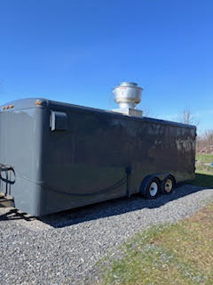 Exterior side view of a dark gray enclosed food trailer parked on gravel with dual axles and rooftop vent.