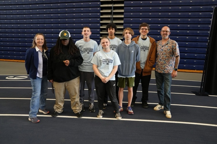  A group picture of Team TST #1 and #2 students and staff stand together in a line inside a gymnasium during the competition.