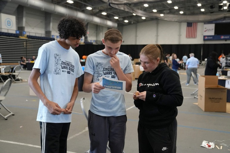 Three students review instructions and materials together while planning their build during the competition.