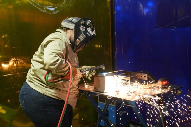 Welder working independently and using a tool to work on a metal box, sparks illuminate the box.