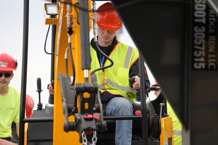  Student wearing a hard hat and safety vest operates heavy equipment controls during a SkillsUSA competition.