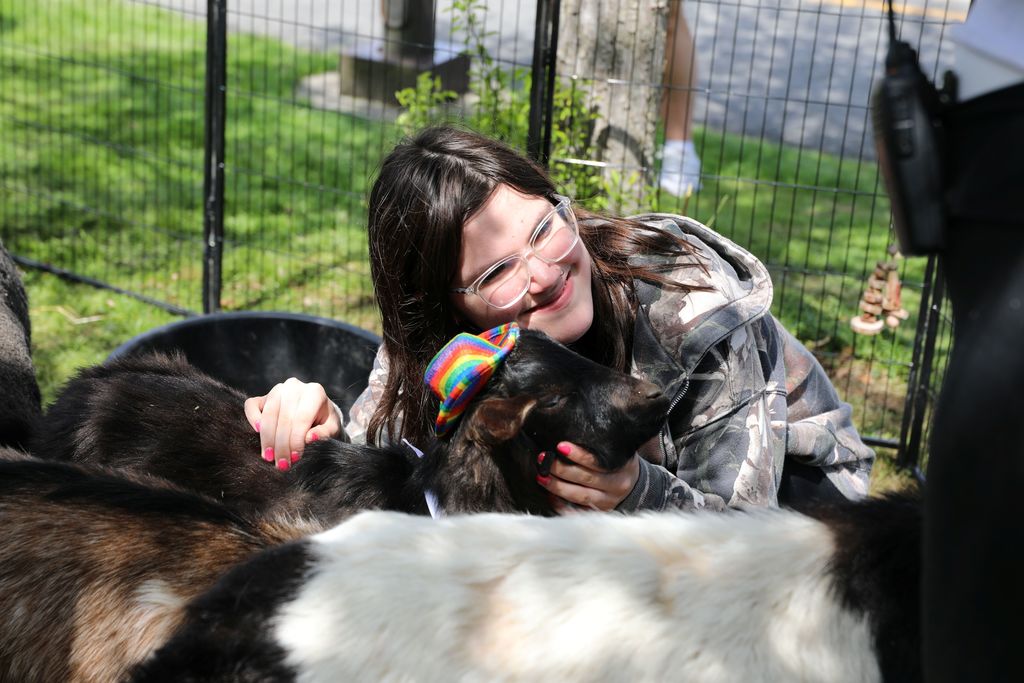 A student posing for a photo with a goat wearing a tiny hat