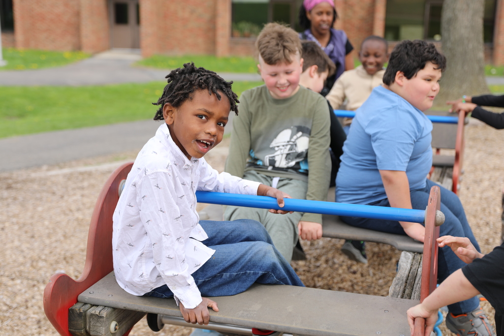 a student smiling at the camera while others in the background play on a seesaw