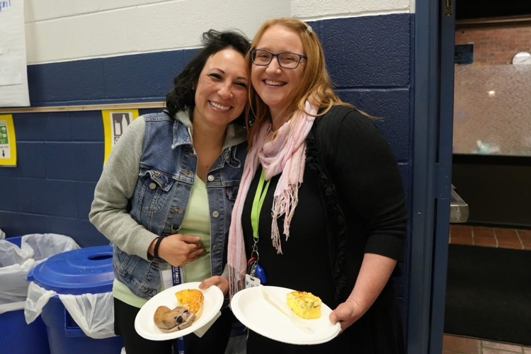 two smith school teachers stand together smiling with full plates in the cafeteria at the staff appreaciation breakfast