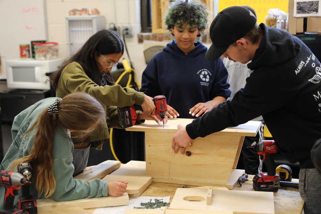 two younger students building a bird house with two older students