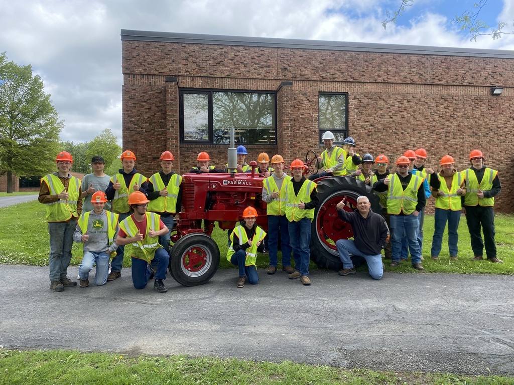 Heavy Equipment students wearing safety vests and hard hats pose with the restored 1949 Farmall tractor outside the TST BOCES CTE building alongside instructor Jeff Brockway.