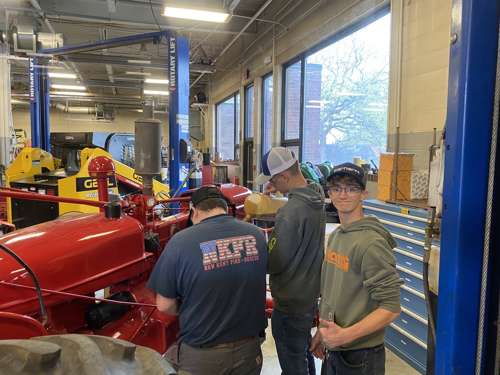 Three students pose beside the nearly completed 1949 Farmall tractor inside the Heavy Equipment shop after restoration work was completed.