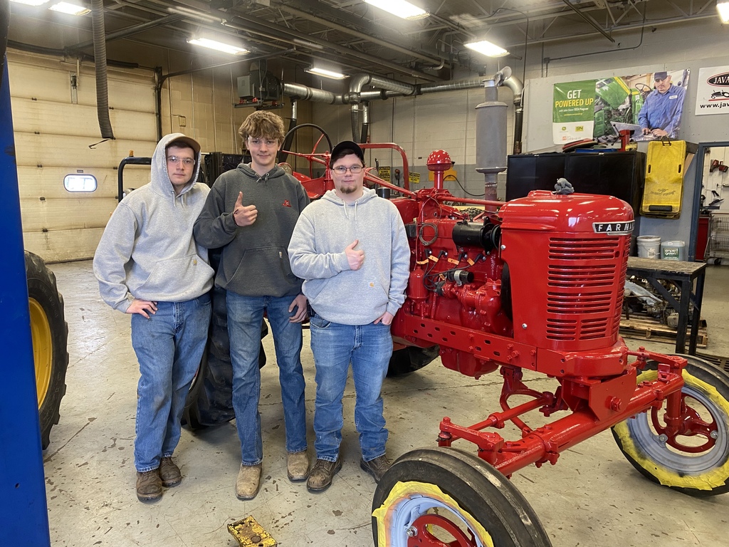 Three students pose beside the nearly completed 1949 Farmall tractor inside the Heavy Equipment shop after restoration work was completed.