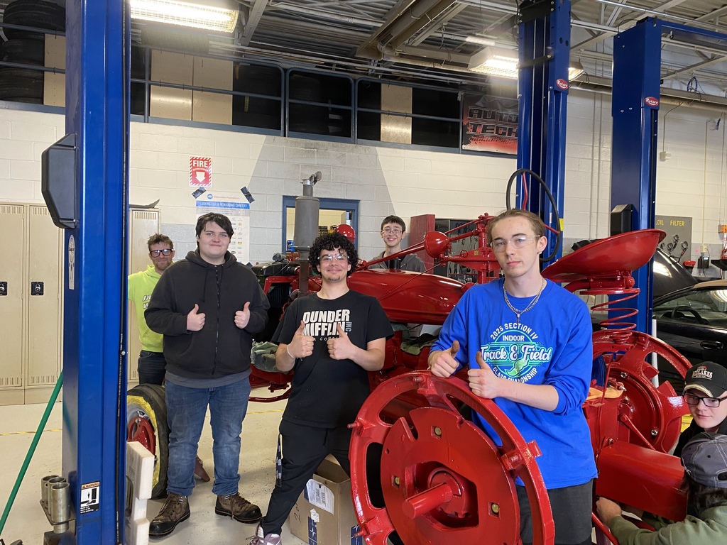 Several Auto Tech students stand around the restored red Farmall tractor inside the shop, smiling and giving thumbs up during the restoration project.