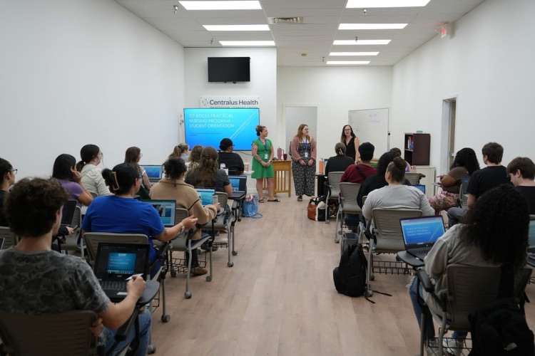 Practical Nursing Program instructors speak to students during orientation at the Centralus Health Professional Learning Center. Students sit at desks with laptops while following along with the presentation.