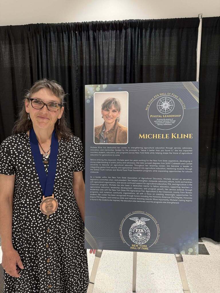 Michele Kline stands beside her New York State FFA Hall of Fame induction display after being recognized for her leadership and contributions to agricultural education.