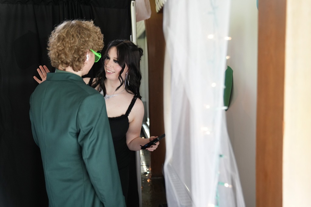 Two students dressed for the dance smile and chat near the themed photo booth decorated with Stranger Things-inspired lights and props.