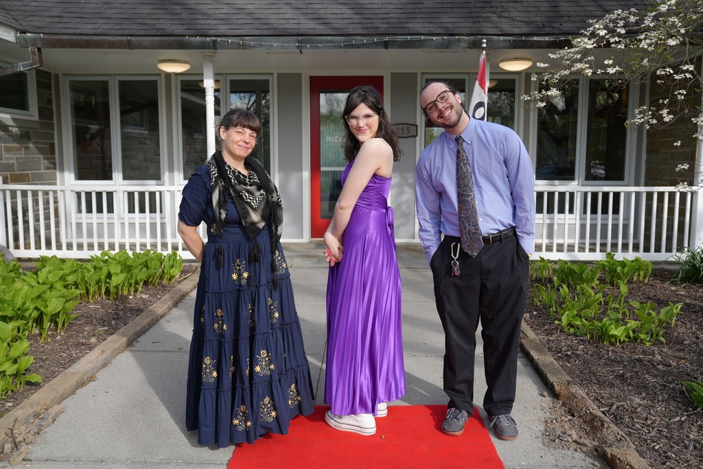 Three attendees pose on a red carpet outside Cornell’s Moakley House before the dinner dance.