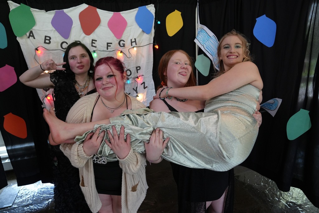 A group of students pose playfully in the themed photo booth while one student is held across the group’s arms.