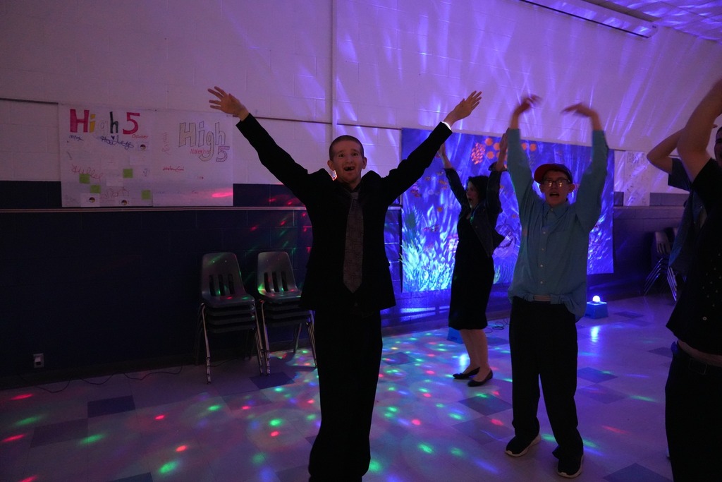 Students dance with their arms raised under colorful disco lights at the Under the Sea themed prom.