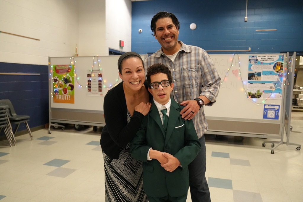 Student in a green suit poses and smiles with two family members inside the decorated prom venue.
