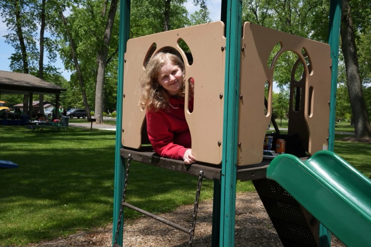 student sticks her head through slide opening at the wow picnic and smile at camera