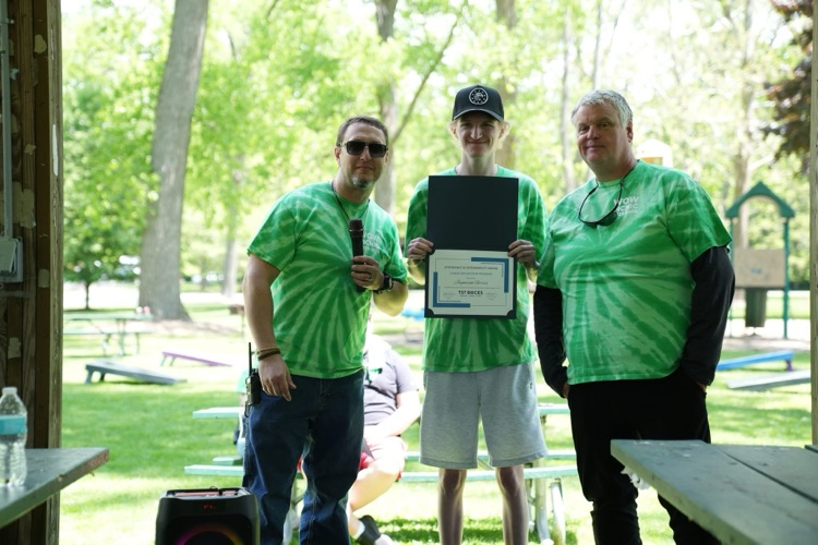 World of Work Career Exploration student stands between two staff members while holding a certificate during an outdoor awards presentation at the annual WOW Picnic.
