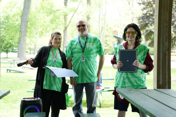 World of Work Outdoor Power student stands between two staff members while holding a certificate during an outdoor awards presentation at the annual WOW Picnic.