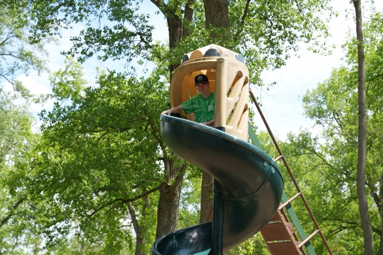 one student sits at the top of the slide smiling toward the camera with trees in the background