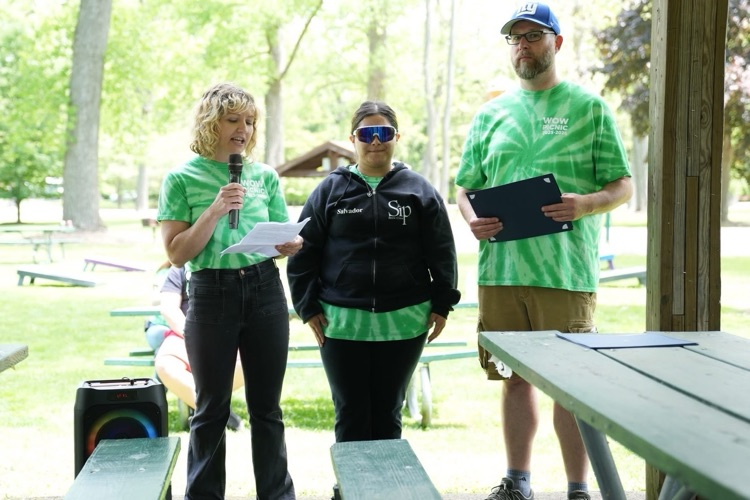 World of Work student stands between two staff members while holding a certificate during an outdoor awards presentation at the annual WOW Picnic from Food Service Class