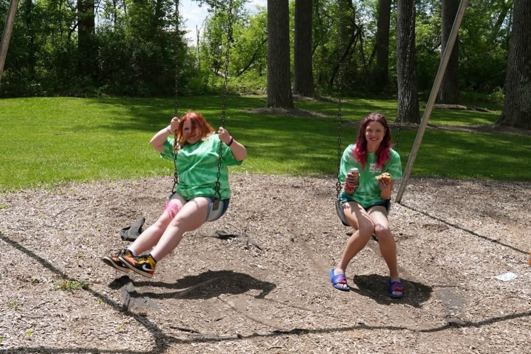 two students swing on the swing set and smile