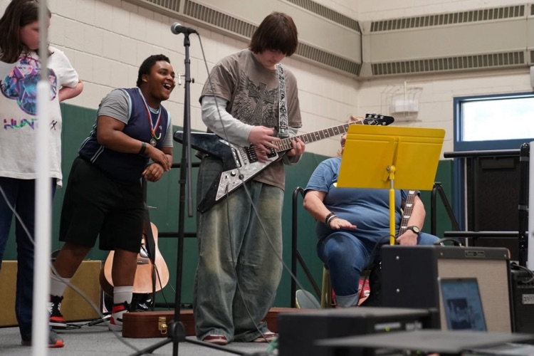 Student plays an electric guitar on stage while classmates and staff look on during a musical performance at Smith School’s Got Talent.