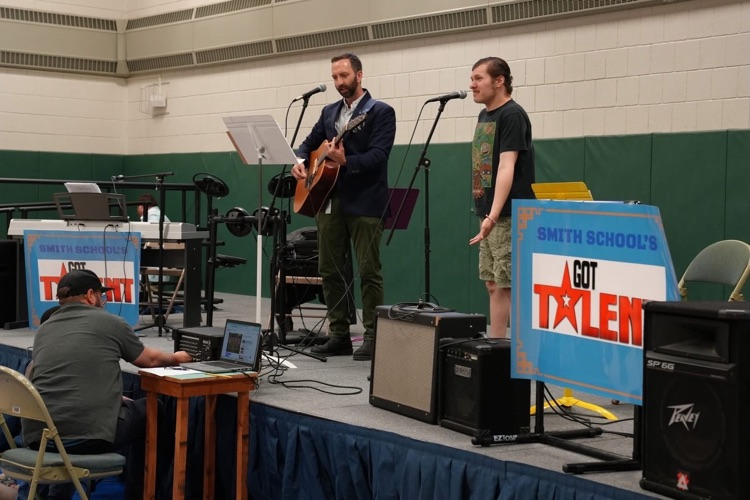 Music teacher plays acoustic guitar and sings with a student standing beside him during a performance at Smith School’s Got Talent.