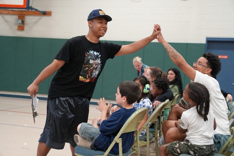 Student gives a high-five to an audience member while walking through the crowd as fellow students watch and applaud during the talent show.
