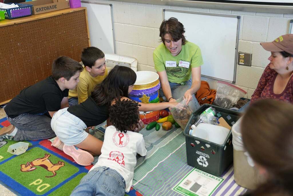 Students gather around a Cornell Cooperative Extension educator as they explore compost materials, food scraps, recyclables, and the composting process.