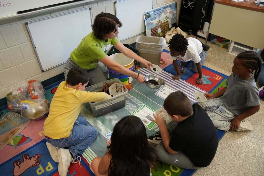 Students work together during a composting activity, examining compost materials and sorting items into categories for recycling, composting, and trash.