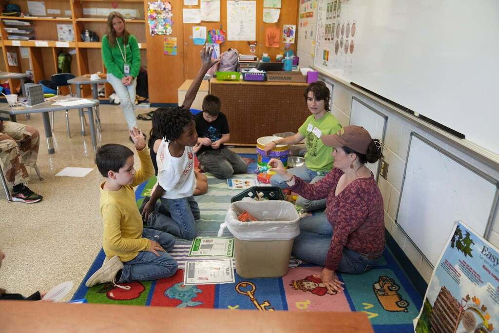 Students raise their hands while participating in a recycling and composting lesson led by Cornell Cooperative Extension educators in a classroom setting.