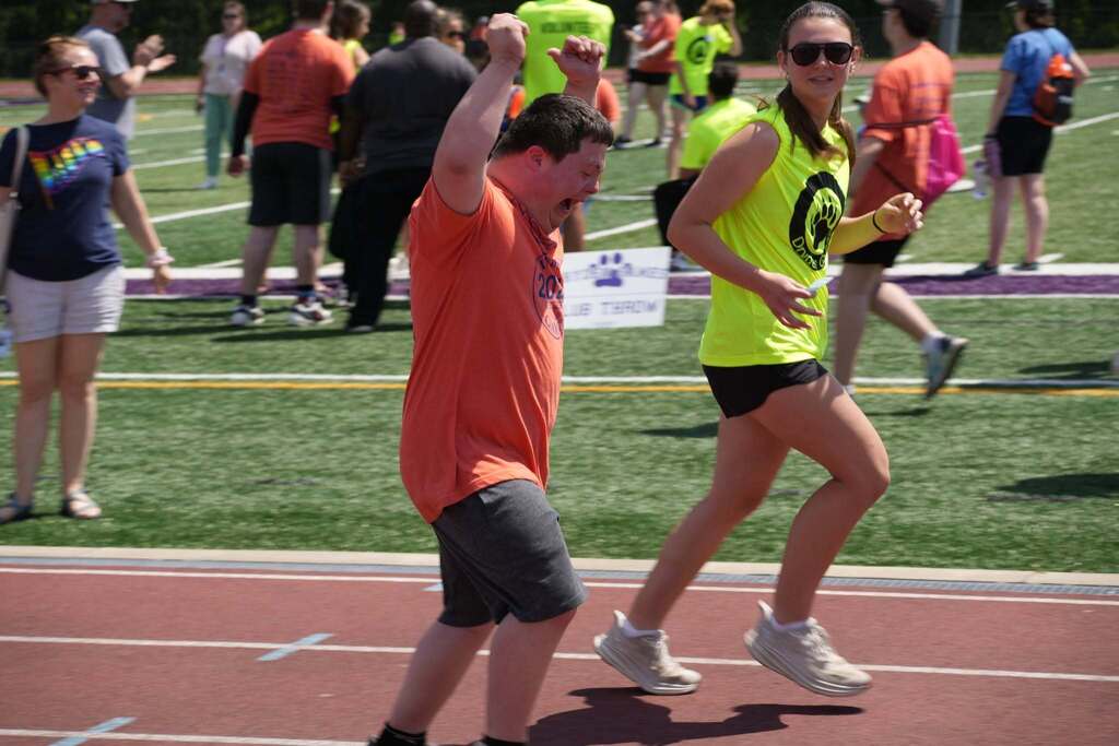 Student celebrates with raised arms while crossing the track alongside a volunteer during a race event.