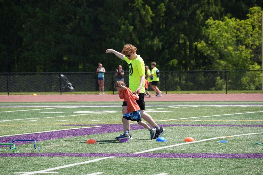 Volunteer assists a young student through an obstacle course activity on the football field during the Dryden Games.