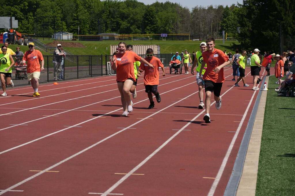 Students sprint down the track during a race while volunteers and spectators cheer from the sidelines.