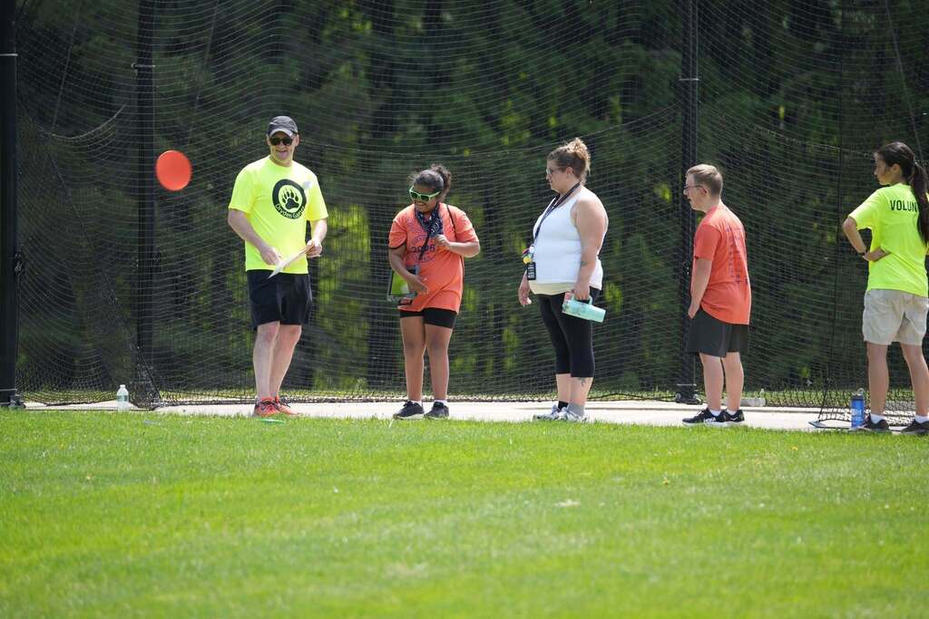 Student prepares to throw a frisbee during a field event as volunteers and staff observe nearby.