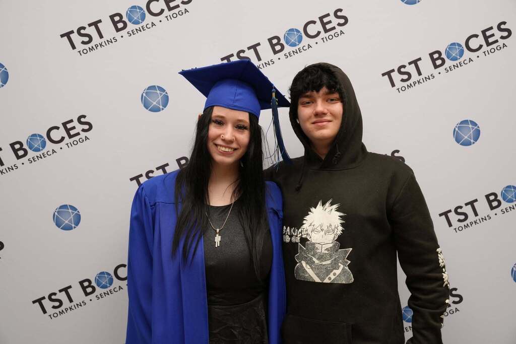 Turning Point graduate in cap and gown poses with a family member in front of a TST BOCES backdrop following the graduation ceremony.