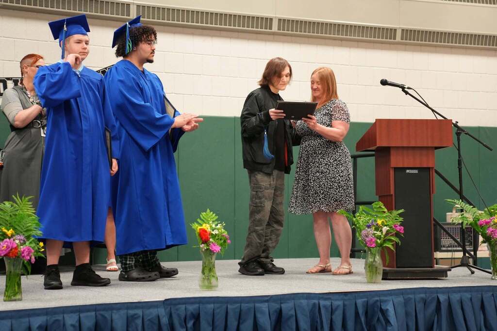 Graduate receives a Circle of Courage certificate on stage during the Turning Point graduation ceremony while fellow graduates wait nearby and applaud.