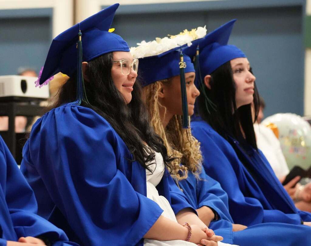 Graduates in blue caps and gowns sit together during the ceremony, listening attentively to speakers and presentations.