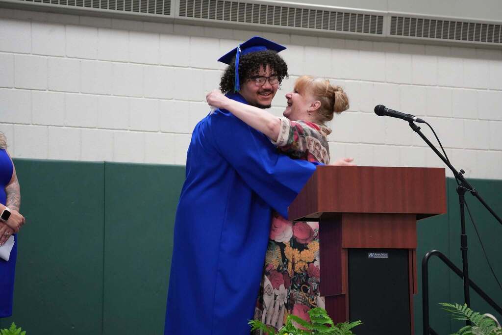Graduate in a blue cap and gown shares a hug with a staff member on stage during the Turning Point graduation ceremony.