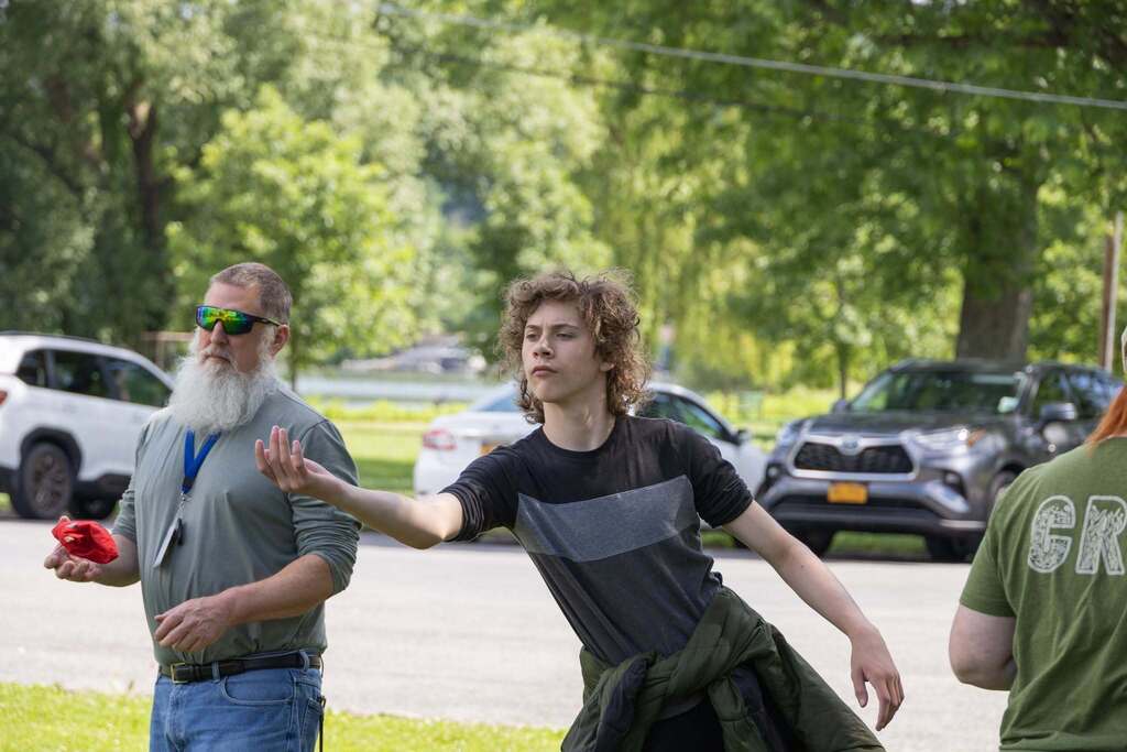 Student tosses a bean bag during a game of cornhole while staff and classmates watch nearby at Stewart Park.