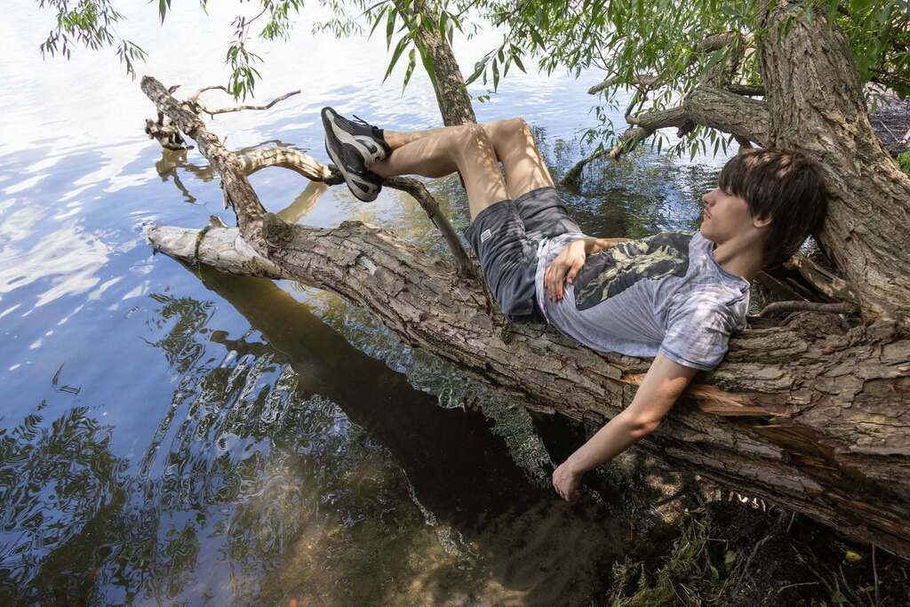 Student relaxes on a large tree branch extending over the water at Stewart Park during the Turning Point BBQ.