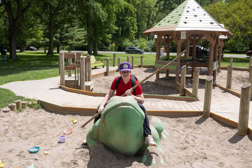 Student smiles while sitting on a large frog sculpture in the playground area at Stewart Park during the Turning Point BBQ.